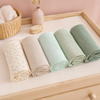 Lot de linges bébé tons verts sur une table à langer