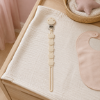Attache-tétine ours beige en silicone sur une table à langer