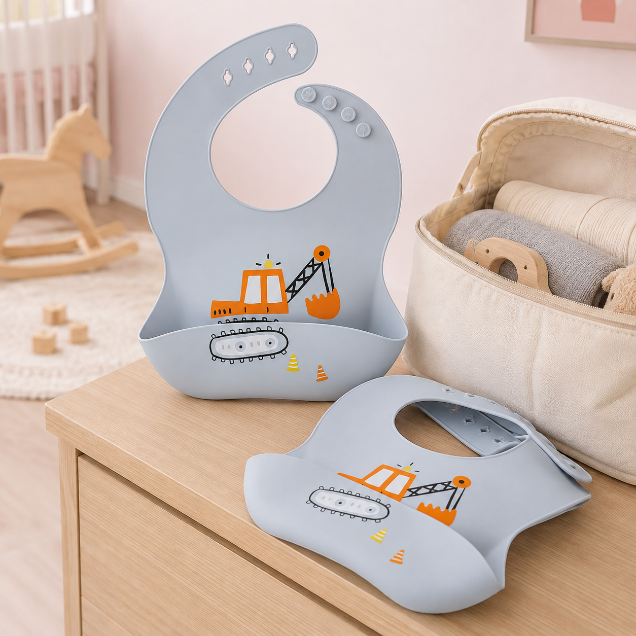 Bavoir bébé en silicone motif pelleteuse près d’un sac à langer