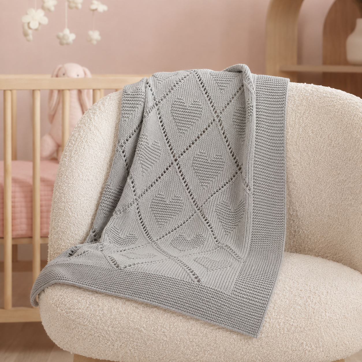 Couverture bébé gris perle en maille à cœurs sur un fauteuil