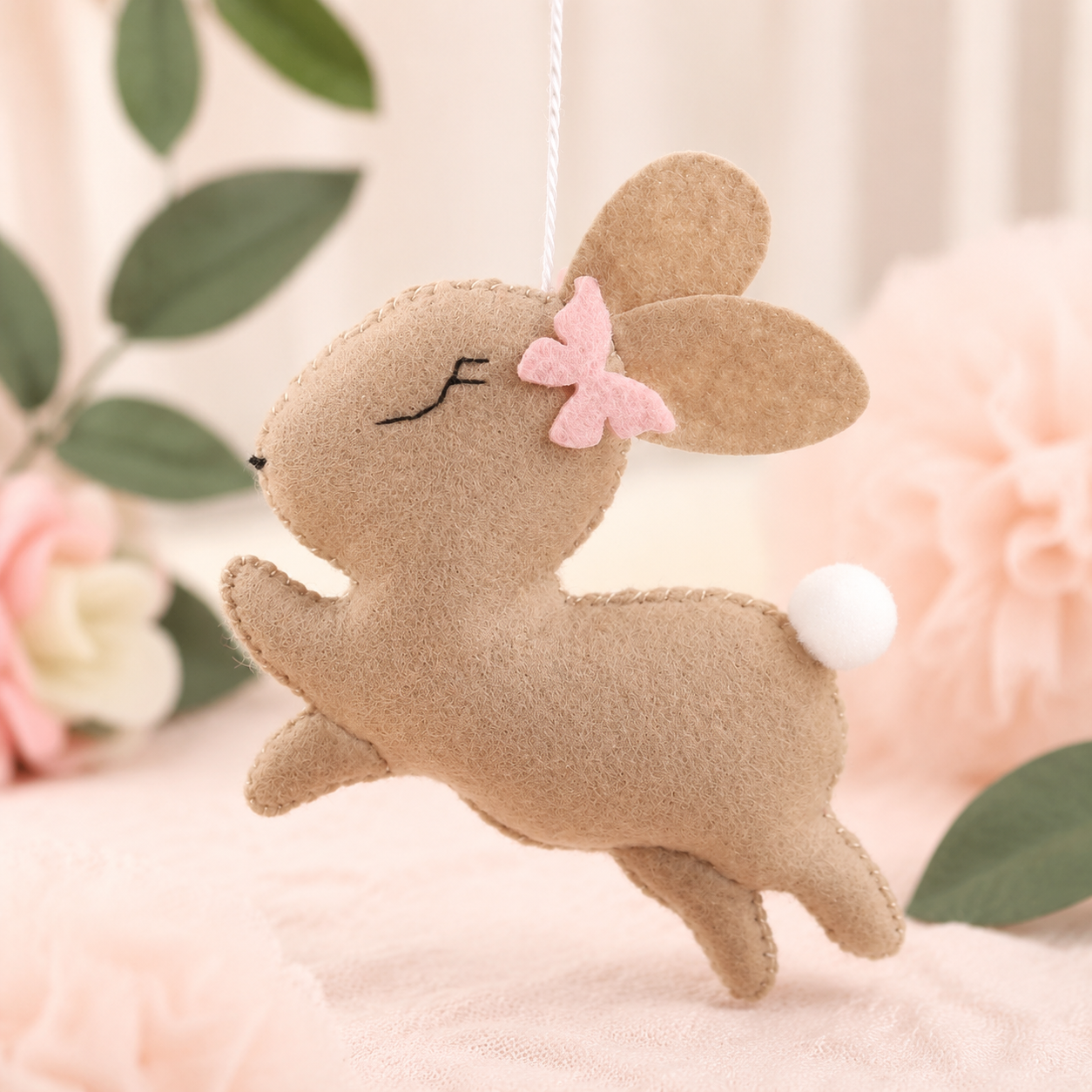 Détail d’un lapin beige en feutrine avec nœud rose